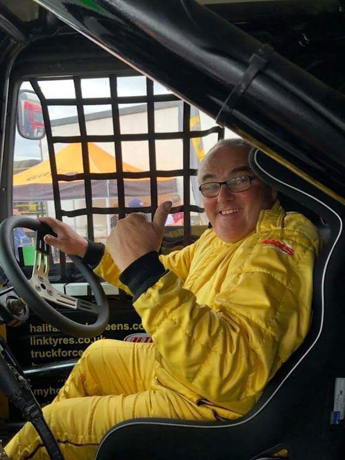 Smiling driver in a yellow race suit giving a thumbs up from a race truck cab