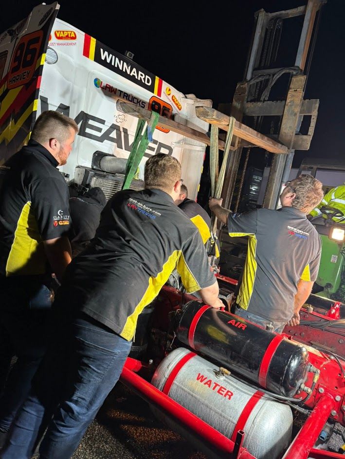 Race team crew lifting the cab of race truck number 96 with a forklift at night