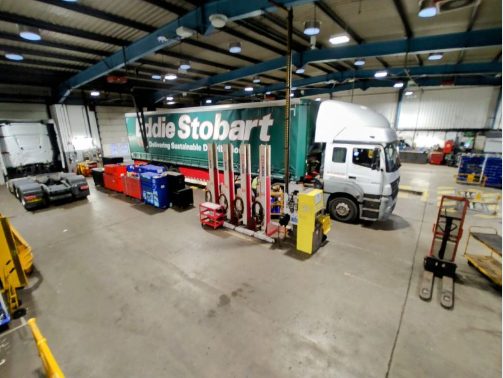 Large commercial vehicle workshop with a curtainside trailer and vehicle lifts