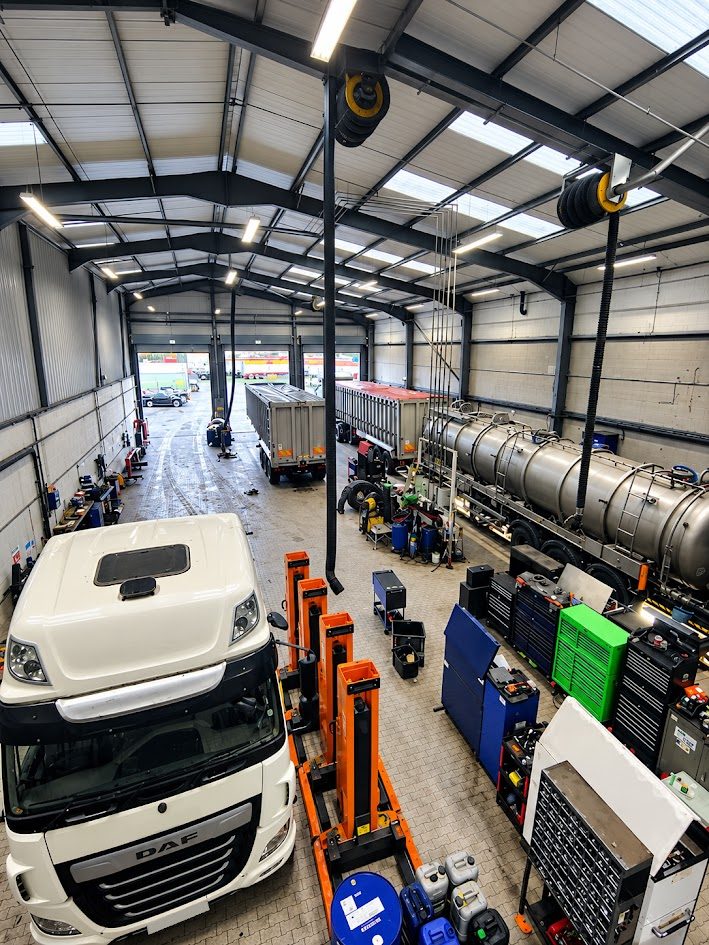 Commercial vehicle workshop with a DAF tractor unit beside mobile column lifts, trailers and a tanker in the bays
